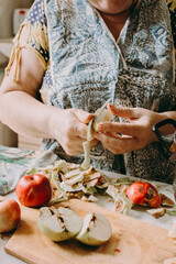Old woman cuts apples for jam. Red ripe apples on the table next to the jam pot. An elderly woman makes jam in her cottage on a farm. Conservation and harvesting. Homemade delicious food