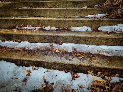 close-up snow melting on rustic weathered concrete stairsteps covered in leaves in early spring. going upstairs perspective with space for copy.
