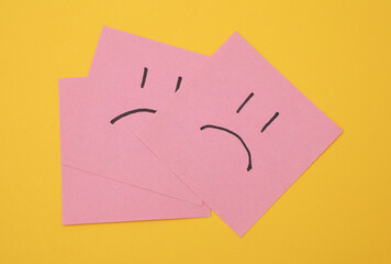Unhappy faces on square memo papers, yellow background. Business concept