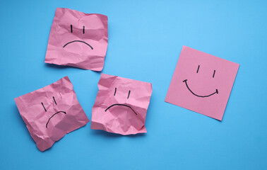 Happy and Unhappy faces on crumpled square memo papers, blue background. Business concept