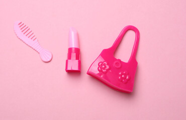 Miniature doll bag with comb and lipstick on pink background. Fashion concept