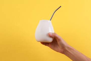 Female hand holding bombilla with white calabash for mate on yellow background. Mockup for design