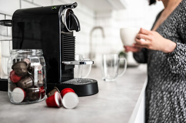 Girl with espresso cup prepared in capsule coffee machine at home. Woman making italian caffeine...