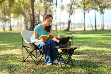 Fototapeta premium A young woman sits playing with a tablet in a quiet park.