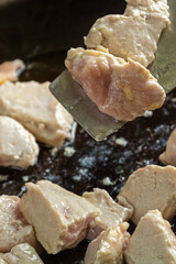 Chicken fillet pieces are fried in a frying pan in oil and turned over