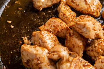 Chicken fillet pieces are fried in a frying pan in sauce and spices