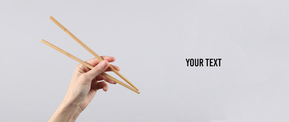 Chinese chopsticks in a female hand on a gray background. Copy space for your text and information