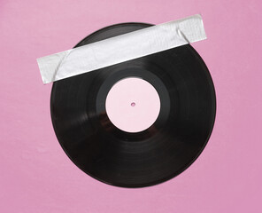 Retro vinyl record fixed with adhesive tape on pink background. Conceptual pop, contemporary art