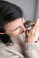Woman hugs a small newborn kitten with tenderness and love