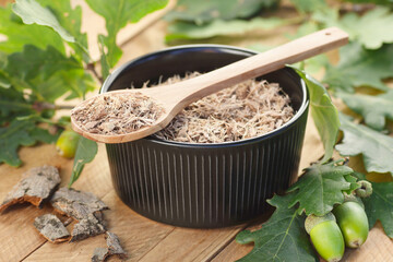Oak bark in a bowl and spoon with leaves on wooden table, closeup, copy space, green medicine,...