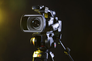 Fototapeta premium Modern video camera with tripod on black background, closeup