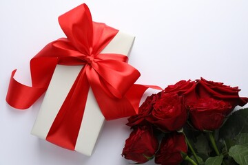 Gift box with red bow and beautiful roses on white background, flat lay