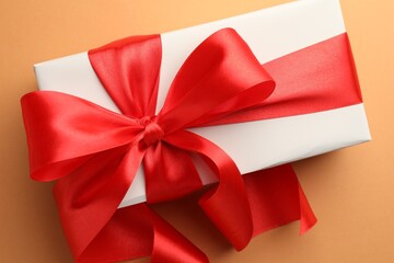 Gift box with red bow on coral background, top view