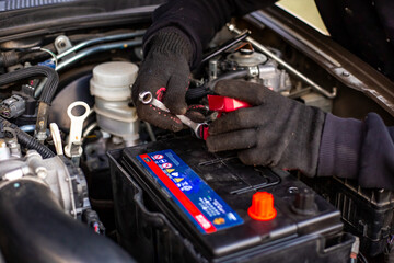 Replacing a car battery. A man installs a battery by tightening the terminals with a wrench under...
