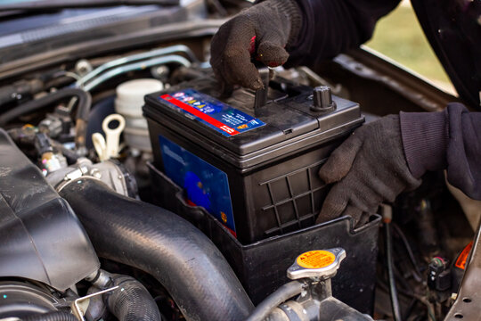 Replacing a car battery. A man installs a battery in a box under the hood of a car
