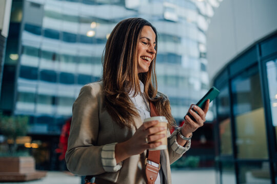 Businesswoman using smartphone and holding coffee outside office building