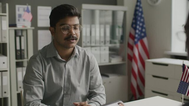 Immigration officer checking US visa application form and interviewing Indian man during formal meeting at consulate. Tilt-up shot
