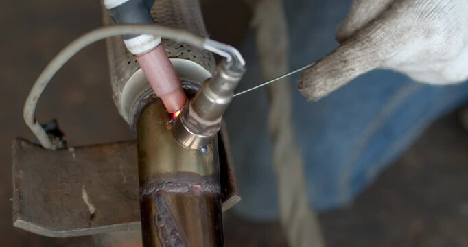 Technician is welding pipe to add position of o2 sensor.Car pipe welding.The hand of a mechanic or welder is fixing a car exhaust system.Tig welding makes the welds come out beautiful.