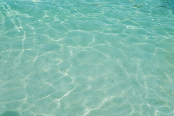 Clear turquoise water, sunlight reflecting, symbolizing natural beauty and serene aquatic scene, bottom through transparent water, blue background, natural resources planet