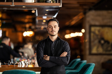 Portrait of professional confident waiter standing in exclusive restaurant with arms crossed.