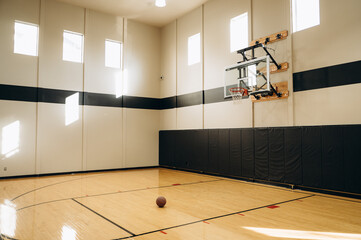 The large wooden gym is equipped for professional basketball, with a basketball and a backboard hanging in the hall.