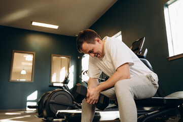 A newcomer to the gym picks up a dumbbell for the first time and lifts it with both hands.