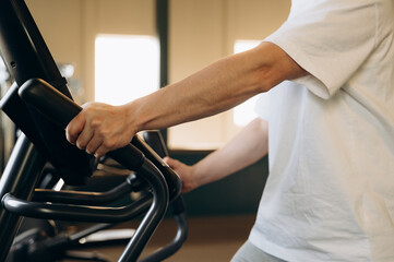 The strong arms of an athlete doing cardio on an elliptical trainer in a state-of-the-art gym with...