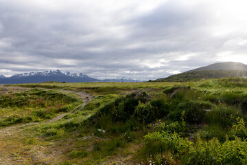A large green field cut through by a marked path on the left side of the image, the landscape is being illuminated by a diffuse light as the sky is a little cloudy.