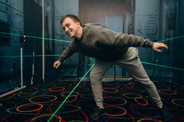 The man carefully bends to avoid the green laser beams. Full concentration and precise movements.