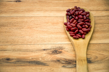 Red beans on wooden spoon over wooden background closeup