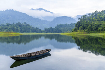 Obraz premium Serene lake with floating boat surrounded by lush mountains and mist