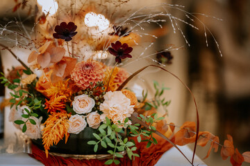 A beautiful floral arrangement with orange and white roses, dried foliage, and greenery, creating an elegant and warm autumn-inspired centerpiece.