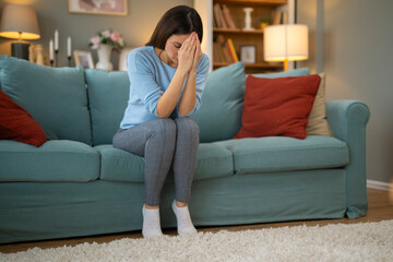 Obraz premium Unhappy woman thinking about problems, sitting on bed in livingroom alone, frustrated young female