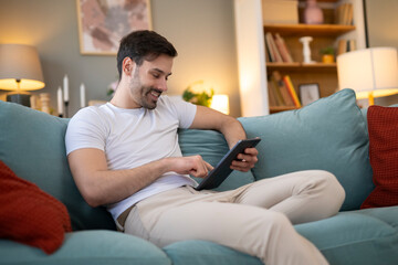 Young man sitting on sofa using digital tablet