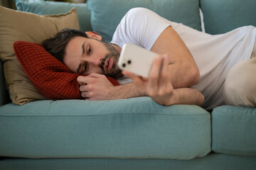 Anxious upset shocked guy in casual lies on couch and holding phone