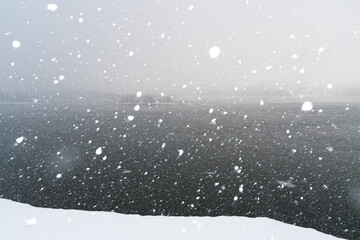 Large white snowflakes on a dark natural background. Snowfall on the shore.