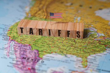 Wooden blocks spelling TARIFFS are placed on a map of North America with USA flag. United states,...