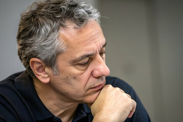 Obraz premium Thoughtful man in contemplation at a desk with a serious expression, capturing a moment of deep reflection and introspection in a modern setting.