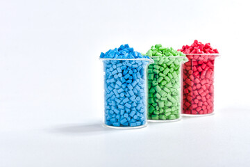 Blue, green and red masterbatch granules in measuring cup isolated on white background, color...