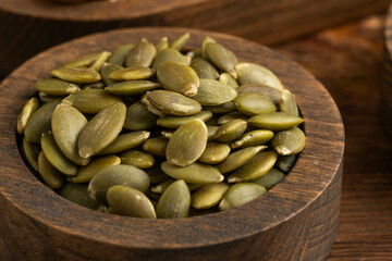 Pumpkin seeds in wooden bowl on wooden background.