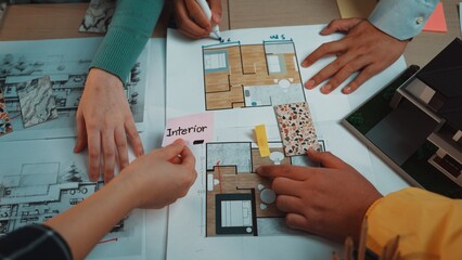 A group of individuals collaborates on interior design plans, showcasing hands selecting color samples and discussing layout details over blueprints and design visuals. SACTR