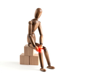 Wooden man sitting on wooden podium with pain in knee.