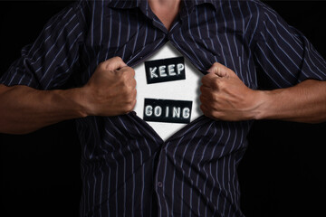 Businessman tearing his shirt revealing word keep going on black background.