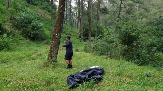 The process of setting up a shelter tent using a flysheet in the forest by a male adventurer. A traveler is setting up a flysheet for a bushcraft adventure in a pine forest area.