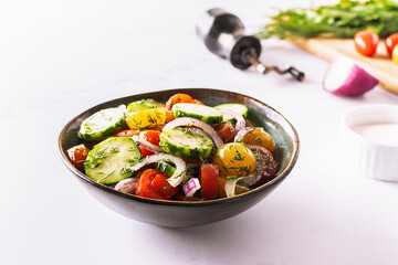 Fresh juicy summer salad with cherry tomatoes, cucumbers, aromatic dill, sweet onion and olive oil in dark ceramic bowl top view. Healthy vegan food concept.