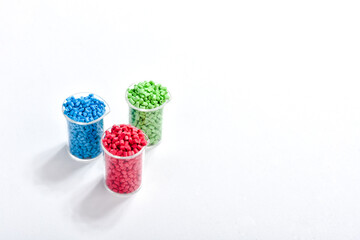 Blue, green and red masterbatch granules in measuring cup isolated on white background, color...