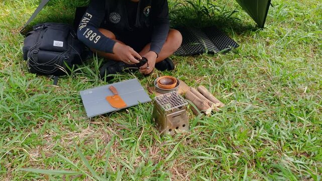 A male adventurer is cooking sauce to make a burger under a flysheet in the dense forest. The concept of bushcraft camping in a dense pine forest for adventure and cooking with simple equipment