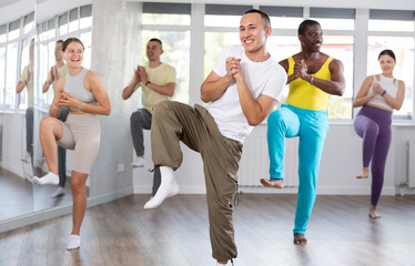 Naklejka premium Young Asian male instructor in casual sportswear enthusiastically guiding diverse class through zumba routine in fitness studio, emphasizing fun and rhythm..