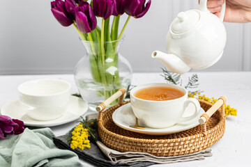 Green tea in a white porcelain cups and teapot, tulips in a glass vase, mimosa flowers, light...