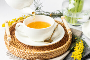 Green tea in a white porcelain cups and teapot, tulips in a glass vase, mimosa flowers, light background. Tea party.
